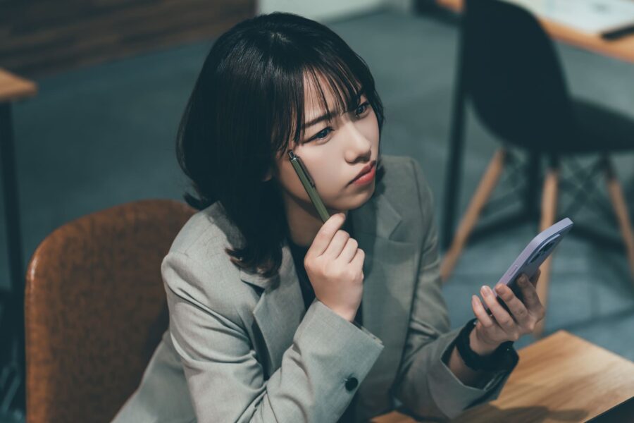 スマートフォンを見ながら不安そうな表情で考え込むスーツ姿の女性
