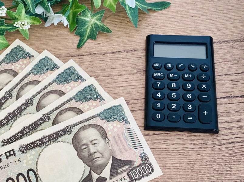 1万円札と電卓が並ぶテーブルの上の写真。GMOバーチャルオフィスの料金プランを説明するコンテンツに関連し、コスト管理や価格比較を連想させるイメージを表現している。